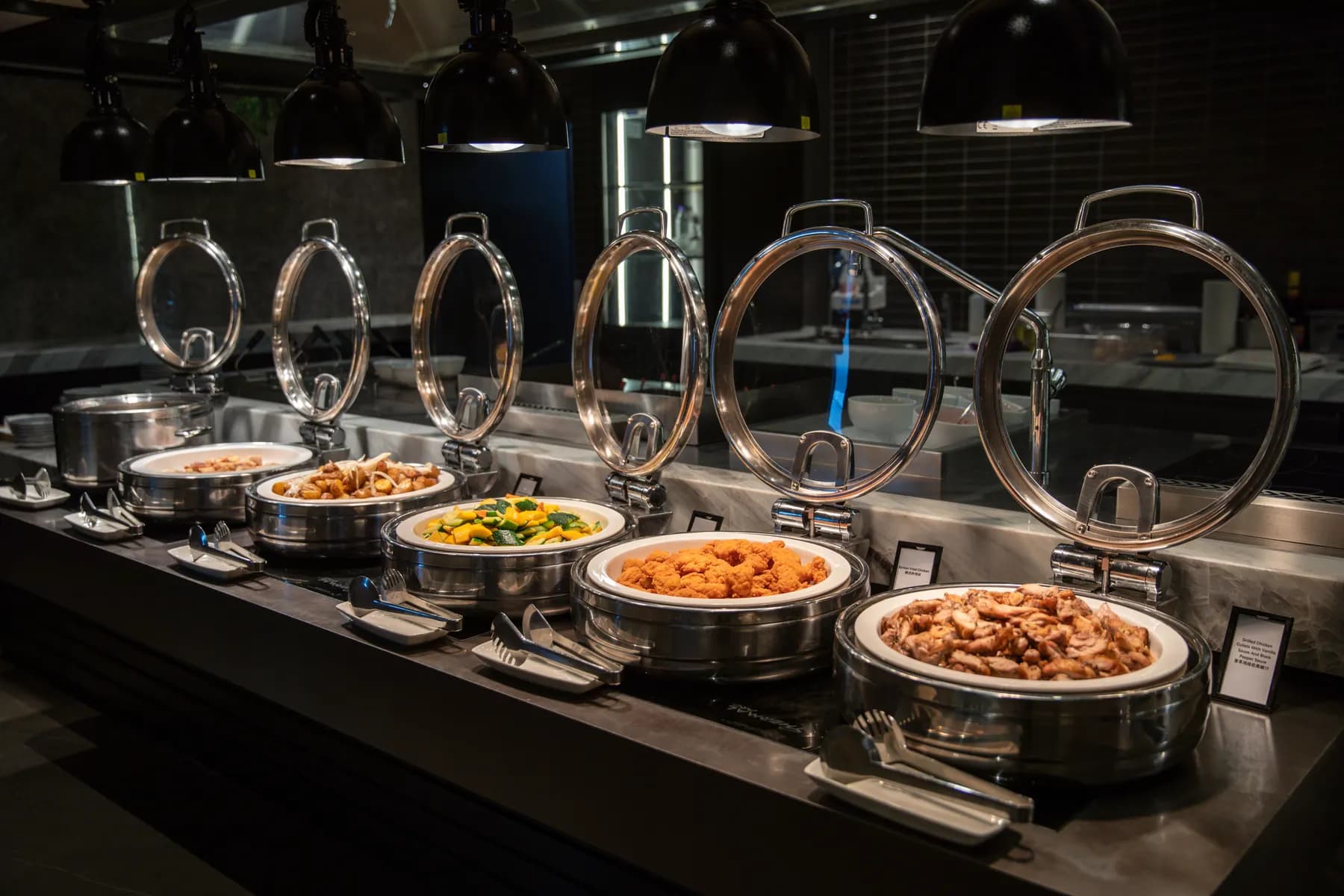 A staffed hot-food bar with covered dishes under warm lights